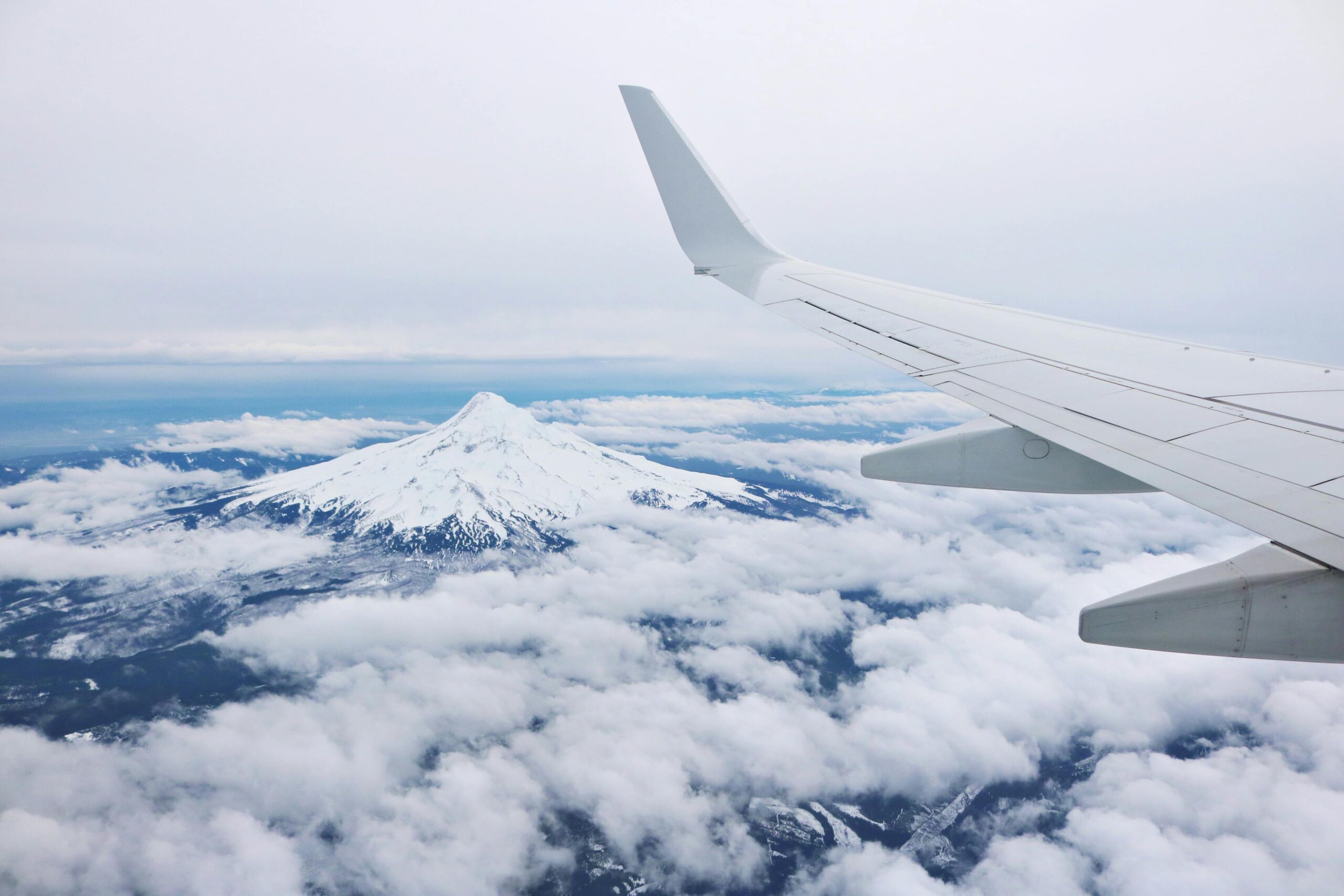 Mountain peak and airplane wing seen from above the clouds, showcasing a beautiful aerial view.